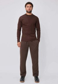 Chemise marron à manches longues associée à un pantalon marron. La tenue présente une coupe slim et est réalisée en matière douce. Les chaussures sont noires.