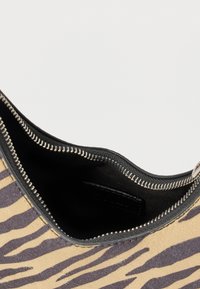 Beżowa i czarna torebka w paski zebry z otwartym srebrnym zamkiem błyskawicznym, odsłaniającym czarne wnętrze z materiału.