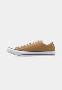 Canvas lage sneakers in tan met witte rubberen teepunt en zool. Voorzien van witte veters en een zwarte streep langs de zool.