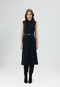 Donkerblauwe mouwloze jurk met een rechte silhouet en een ronde hals, getailleerd met een bruine riem met een decoratieve gesp.