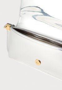 Ασημένια μεταλλική τσάντα φάκελος με λεία υφή, διαθέτει χρυσό κούμπωμα και τσέπη με φερμουάρ. Το εσωτερικό είναι επενδεδυμένο με σκουρότερο υλικό.