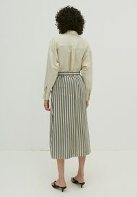 Beige shirt met lange mouwen en een rugpas, gecombineerd met een zwart-wit gestreepte midi-rok met een elastische tailleband en een relaxed fit.