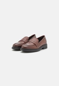 Mocassins en cuir marron avec une finition lisse, présentant une couture et une semelle en caoutchouc noir basse. Design classique avec un style à enfiler.