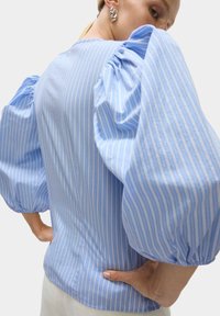 Bluse mit blauen und weißen Streifen, voluminösen Puffärmeln und tailliertem Brustbereich. Hergestellt aus weichem Stoff mit glatter Textur.