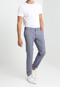 Pantaloni azzurri a motivo con una vestibilità rilassata, dotati di chiusura a bottone e cerniera, con risvolti, indossati con una maglietta bianca semplice e sneaker bianche.