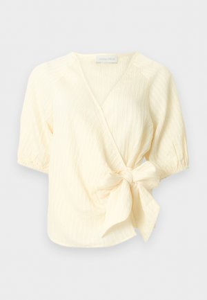 Kreminės spalvos trumpomis rankovėmis užtraukiama palaidinė su V formos iškirpte ir tekstūruota medžiaga, su dideliu šoniniu kaspinu ir elastiniais rankovių manžetais.