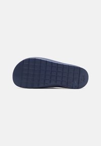 Semelle en caoutchouc marine avec un motif texturé en grille et un talon arrondi. Présente un logo estampé sur le côté.