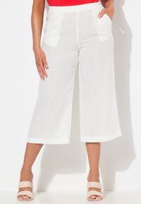 Pantalons larges blancs en tissu texturé, avec une taille élastique et deux poches avant, associés à des sandales légères tressées.