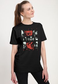 Czarny t-shirt z nadrukiem graficznym przedstawiającym czerwone i białe obrazy w stylu horror oraz tekstem "WRÓĆ I GRAJ". Krótkie rękawy i okrągły dekolt.