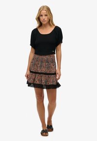 Sort cropped top og mønstret mini nederdel i orange og blå nuancer. Nederdelen har en blondekant og smocked talje. Flade sandaler fuldender looket.