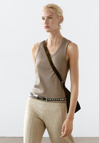 Bruine geribbelde tanktop, zwarte gesp studded riem, lichtbeige gestreepte broek en een schoudertas. Het model heeft steil haar en minimale accessoires.