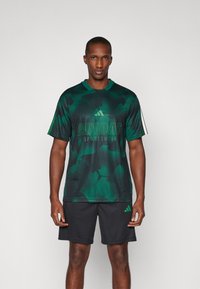 Κοντομάνικη αθλητική μπλούζα Adidas σε πράσινη παραλλαγή με στρογγυλή λαιμόκοψη και μαύρη βερμούδα, με λογότυπο σε αντίθεση ζωηρού πράσινου.