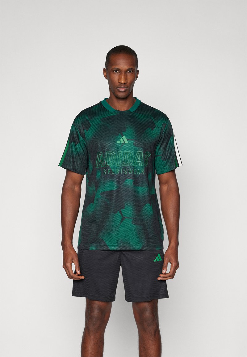 Κοντομάνικη αθλητική μπλούζα Adidas σε πράσινη παραλλαγή με στρογγυλή λαιμόκοψη και μαύρη βερμούδα, με λογότυπο σε αντίθεση ζωηρού πράσινου.