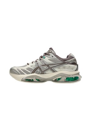 Scarpa da corsa grigio chiaro e beige con tomaia in mesh, dettagli marroni e ammortizzazione visibile con accenti verdi nella suola.