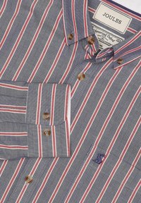 Vyriška mėlyna Oxford tipo marškiniai su raudonomis ir baltomis juostelėmis, rudos spalvos mygtukais ir siuvinėtu logotipu šalia krūtinės kišenės.