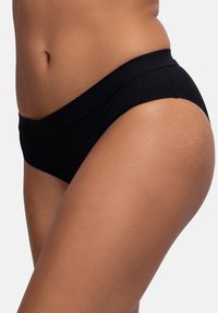 Juodas bikini apatinis trikotažas su griovelių tekstūra, turintis platų juosmenį ir vidutinę aprėptį. Matomos šoninės siūlės, audinys atrodo elastingas.