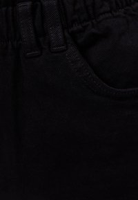 Tejido negro con una cintura elástica fruncida y un bolsillo delantero, con una superficie suave y texturizada y detalles de costura visibles.