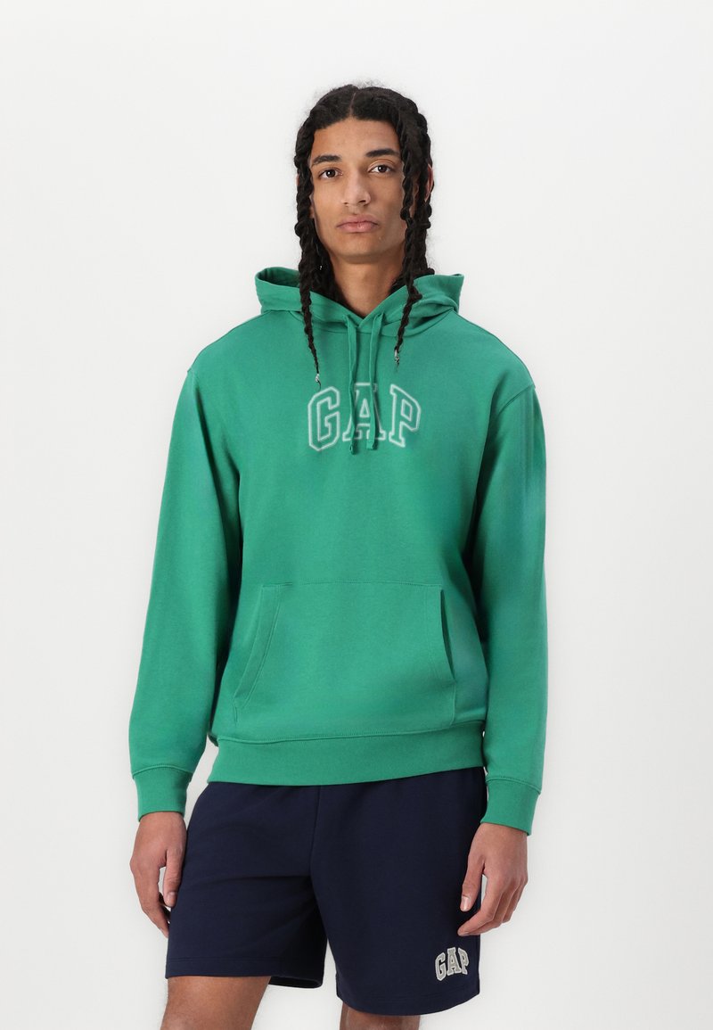 Žalias kapisonas su raišteliais, kengūros kišene ir "GAP" logotipu. Minkšta medžiaga, susukti rankogaliai, derinamas su tamsiai mėlynomis šortais.