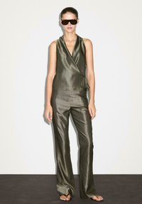 Olivgrön ärmlös omlott-topp med knytning i midjan och matchande vida byxor, båda med en slät, glansig yta.
