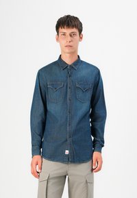 Camisa de mezclilla, azul oscuro, de mangas largas, con botón en la parte delantera, dos bolsillos en el pecho con solapa, textura sutil, etiqueta en el dobladillo inferior, corte estándar.