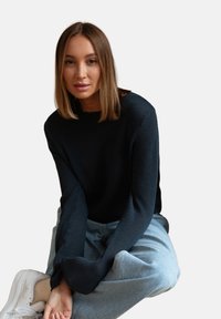 Czarny sweter z dzianiny z długimi rękawami, noszony z jasnoniebieskimi spodniami typu wide-leg. Stylizację dopełniają białe trampki.