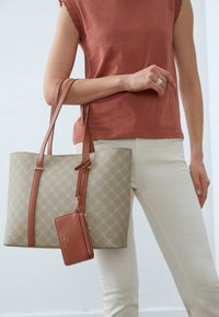 Beige kantokassi, jossa on kuvioitu pinta, ruskeat nahkakahvat ja siihen kiinnitetty matching-pieni lompakko. Rakenteellinen yksityiskohtaisuus ja tyylikkäämpi muotoilu.