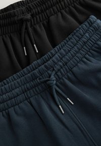 Schwarze und dunkelblaue Jogginghosen mit elastischem Bund und Kordelzügen. Glatter Stoff mit glänzenden Metallspitzen an den Kordelzügen.