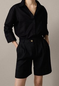 Svart skjorta med knappar framtill, krage, lös passform och uppvikta ärmslut, kombinerad med skräddarsydda svarta shorts med framknäppning och veck.