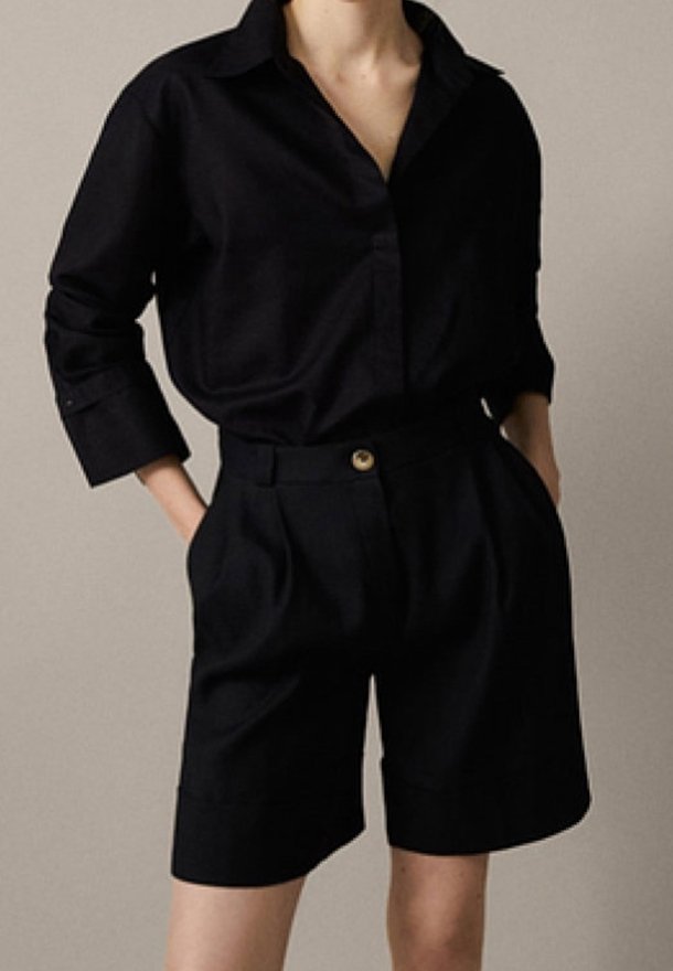 Svart skjorta med knappar framtill, krage, lös passform och uppvikta ärmslut, kombinerad med skräddarsydda svarta shorts med framknäppning och veck.