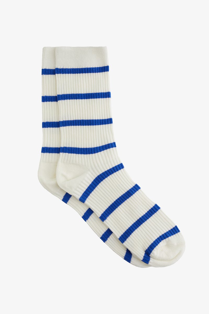 Baltos raišteliais kojinės, išsiskiriančios ryškiomis mėlynomis horizontaliosiomis juostelėmis. Dizainas apima sustiprintą kojų ir kulno dalį ilgaamžiškumui.