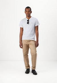 Stripet skjorte med kort erme i hvit og marineblå, beige chinos og svarte sko. Solbriller ligger på skjorten, subtil logo detalj på brystet.