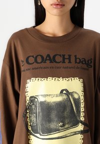 Ruskean suurikokoinen t-paita, jossa musta teksti ja keltainen ääriviiva vintage-repusta. Sujuva rakenne, rento istuvuus.