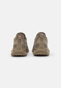 Baskets en mesh beige avec une semelle en caoutchouc texturé, un col rembourré et deux tirants à l'arrière pour un enfilage facile. Présente un branding subtil sur le côté.