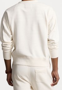 Krämfärgad sweatshirt med en avslappnad passform, ribbstickade muddar och nederkant. Slät textur med en liten rektangulär etikett på baksidan.