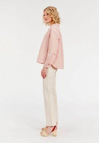 Haut rayé rose clair à manches longues associé à un pantalon taille haute beige. Des sandales chunky beiges avec des accents rouges viennent compléter la tenue.