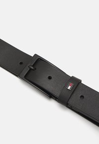 Cintura in pelle nera con finitura opaca, dotata di una fibbia rettangolare nera e un piccolo logo accentato in rosso, bianco e blu.