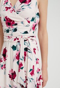 Blumiges Wickelkleid mit einem hellrosa Hintergrund und lebhaften roten und grünen Blumen, einem taillierten Gürtel und weichem, leichtem Stoff.