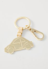 Auksinis metalinis raktų pakabukas, primenantis automobilį, su tekstūruota odos akcentu ir užsegimu tvirtinimui. Lygūs paviršiai su aiškiai apibrėžtomis kontūromis.