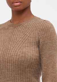 Pull en maille côtelée marron avec un col rond, présentant des lignes verticales et une texture douce. Gros plan mettant en avant le détail du tissu.