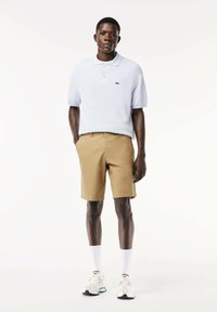 Polo shirt azzurro con un piccolo logo verde, abbinato a pantaloni corti color khaki. Il modello indossa calze bianche e scarpe da ginnastica multicolori.