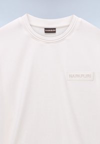 Camiseta blanca de cuello redondo con un pequeño parche rectangular con el logo de Napapijri en el lado izquierdo del pecho y una etiqueta negra en el interior del cuello.