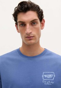 Sweatshirt din bumbac albastru cu guler rotund, având o grafică albă cu un pește și textul "Felul zilei" pe partea stângă a pieptului.