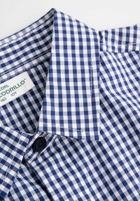 Niebiesko-biała koszula w kratę vichy z kołnierzykiem na guziki, z pojedynczym guzikiem przy szyi oraz miękką, lekką tkaniną.