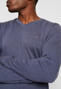 Pull-over à col en V en marine chiné, texture en maille, avec un petit logo sur la poitrine. Manches longues avec des poignets ajustés.