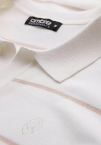 Polo shirt van witte stof met lichtroze horizontale strepen, voorzien van een getextureerde kraag en een reliëflogo dichtbij de zoom.