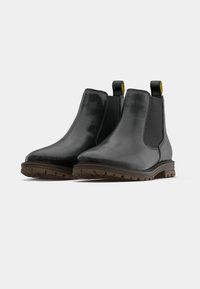 Botas Chelsea pretas em pele com painéis laterais elásticos, alças de puxar e solas de borracha texturizadas para melhor aderência. Acabamento liso e design minimalista.
