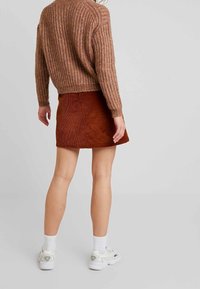 Pull en tricot marron à texture côtière, associé à une mini-jupe en velours côtelé rouille. Le mannequin porte des baskets blanches et des chaussettes à la cheville.