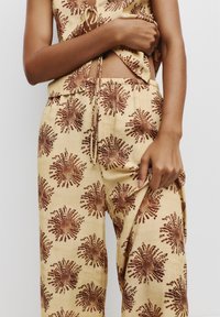 Beige outfit met een strakke top met een strik en uitsnijding, gecombineerd met losse broek met een roodbruine bloemenprint.