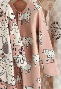 Trois vêtements pour bébés zippés : rose pastel avec imprimé animal à pois, crème avec illustrations d'animaux, et beige à carreaux avec un graphique. En matériau coton.