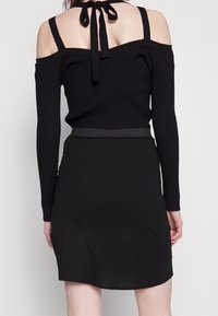 Top nero a coste off-the-shoulder con maniche lunghe e dettagli legati sulla schiena, abbinato a una gonna nera aderente. Texture liscia.